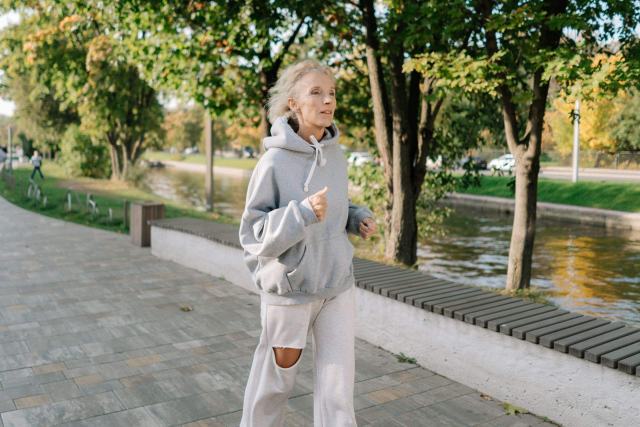 Femme qui court le long d'un canal dans un parc, tenue de sport et capuche grise